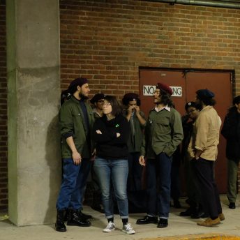 Director Emma Francis-Snyder talking to an actor, behind of them there are more actors, they are all in front of a door