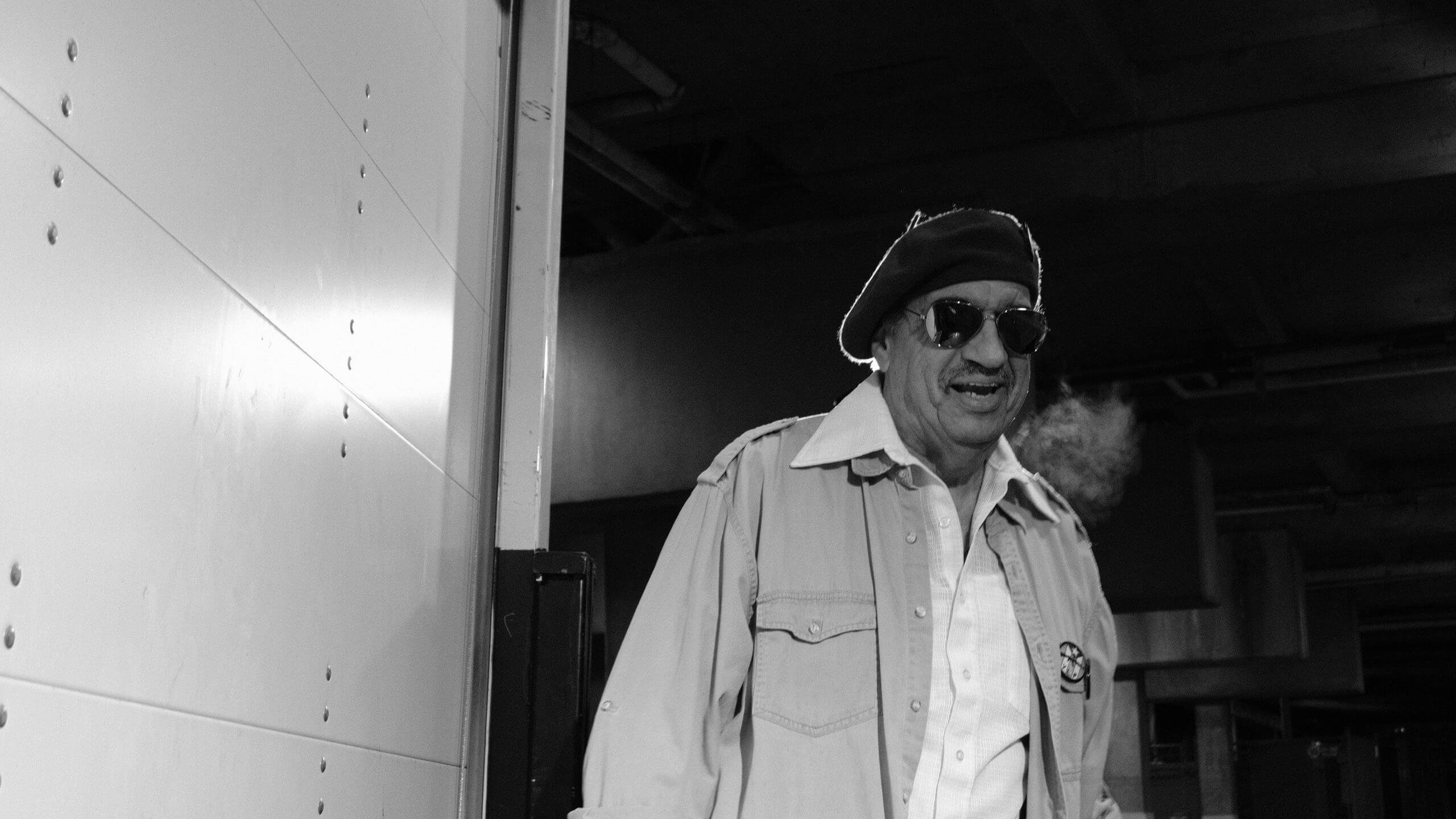 Low angle shot of an actor, wearing a shirt, a jacket, a beret, and dark glasses