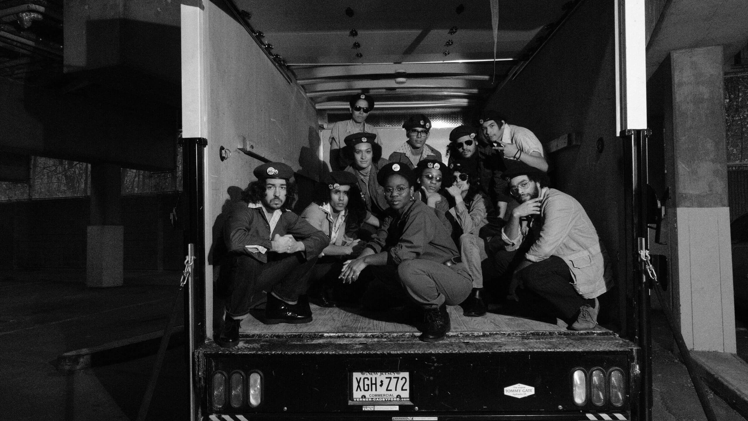 A group of actors dressed as members of the Young Lords Party inside of the back of a trailer truck, looking at the camera