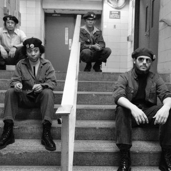 Low angle shot of four actors dressed as members of the Young Lords Party sat on a stair