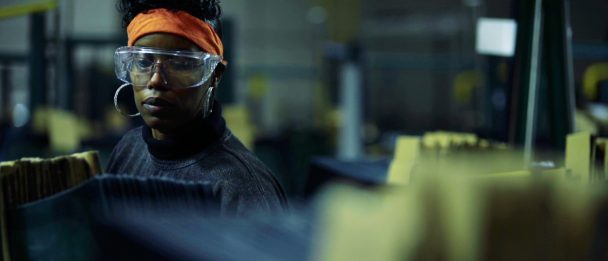 Still from American Factory. A worker wearing protective glasses works with a machine that is out of focus.