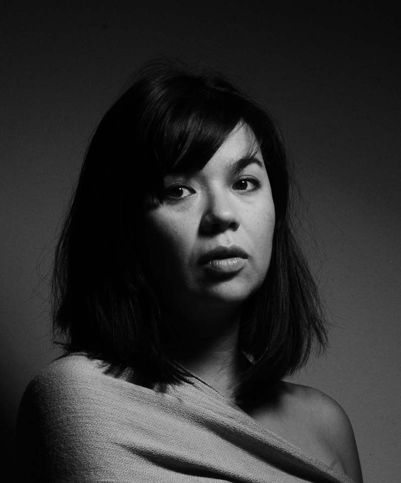 Kiyoko McCrae looks directly at the camera. Portrait in black and white.