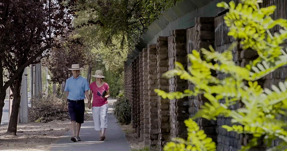 Still from The Eternal Memory. Augusto and Paulina holding hands and walking down a lane, both wear hats.