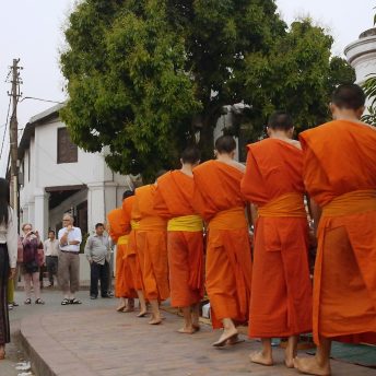 A line of monks on the right and tourists takin pictures to them on the other side.