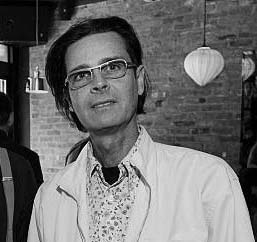 Man with dark hair and glasses wears white jacket.