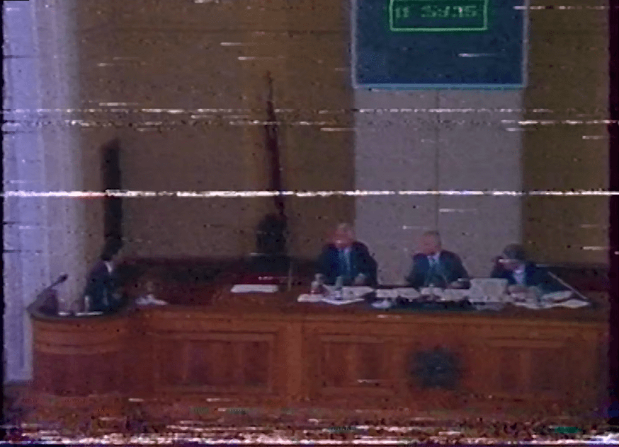 Damaged VHS archive image of four people at the wooden Parliament podium