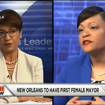 Still from All Skinfolk Ain't Kinfolk. Two women are on opposite sides of the screen, one in a white jacket and a blue jacket. At the bottom of the screen text states that New Orleans is to have its first female mayor.