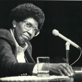 A black-and-white image of a Barbara Jordan with an afro in front of a microphone
