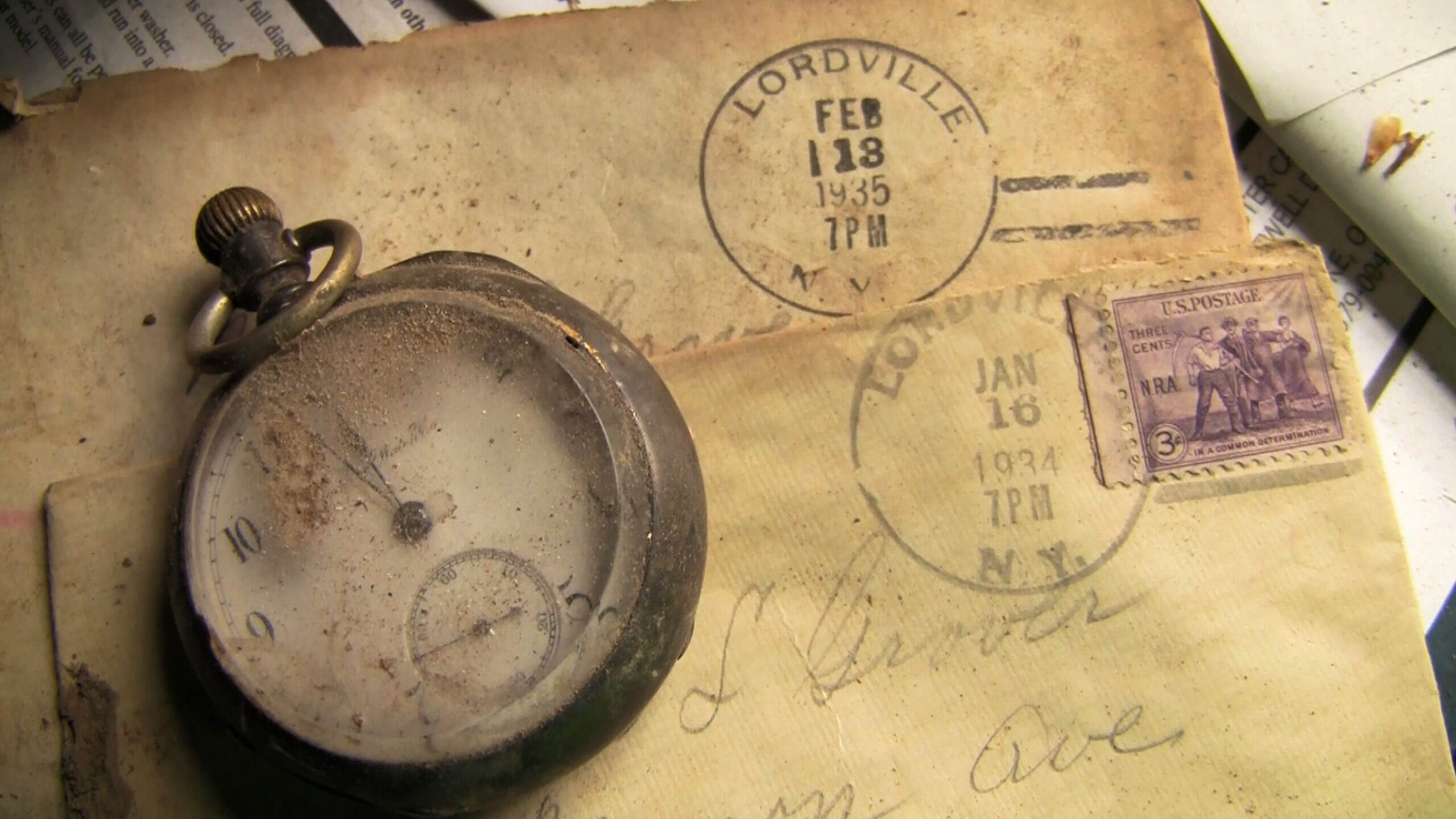 Still from Lordville. A closeup of a dirt encrusted antique watch that sits on top of a yellowed old letter with a postmark dated to February 13, 1939, Lordville New York.