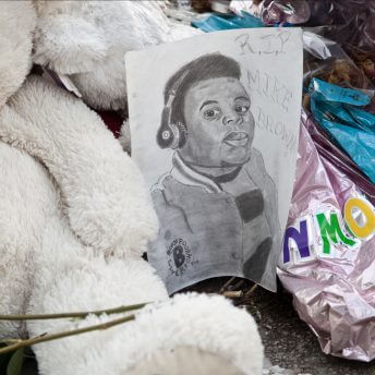 Still from Whose Streets?. A street memorial featuring a hand drawn sketch of Mike Brown Jr. The sketch is resting against a large white teddy bear and several deflated balloons