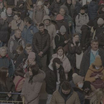 Still from Displaced. Hundreds of people are standing at the main railway station waiting for evacuation trains. The camera is placed at a high angle and captures their worried expressions.