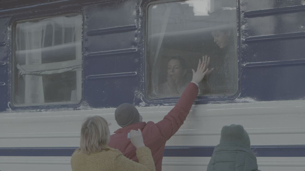 Still from Displaced. A man is saying goodbye to his wife and son through the window of the train. His hand reaches to the window from the train station platform as his family looks down.