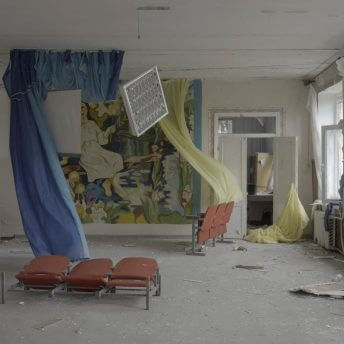 Production still of Intercepted. A ransacked classroom in a school near Mikholaiv is shown. Blue and yellow cloths are hanging from the ceiling, a light fixture is hanging from the ceiling by a thread. The classroom door is wide open and wind is blowing from the destroyed windows