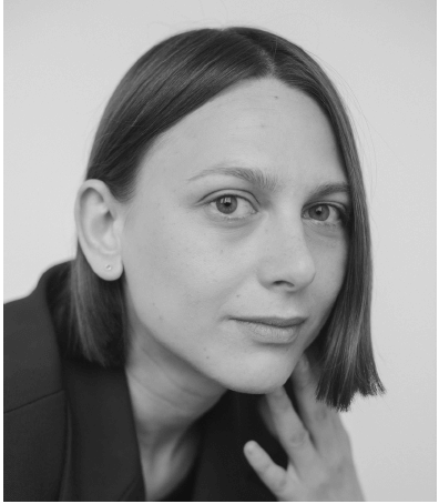 Oksana Karpovych looking directly at the camera. She has short brown hair and has her hand close to her face. Black and white portrait.