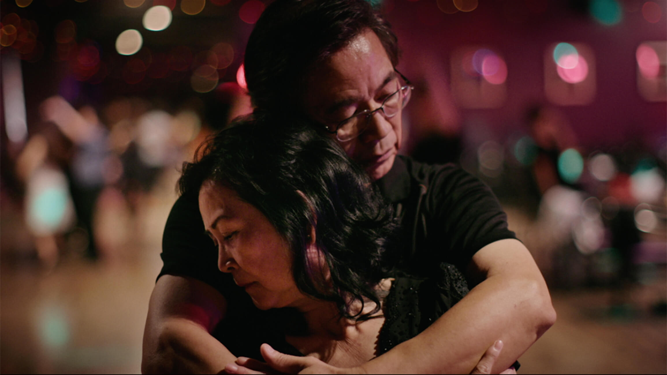 Middle aged Asian man wearing glasses embraces middle aged Asian woman.