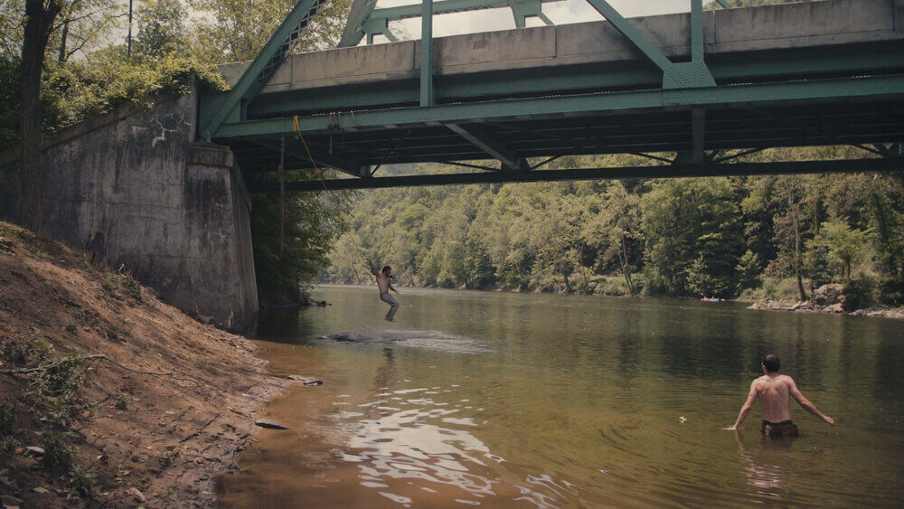 A man swings from a rope into a river.