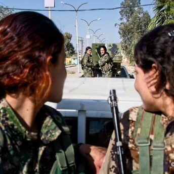 Two guerilla women in a car look behind them at other guerillas and smile.