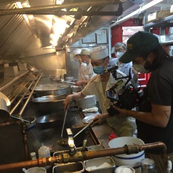 Cinematographer Nate Brown filming chefs in the kitchen of Hop Kee restaurant