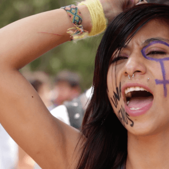 Fany with her face painted with a feminist symbol shouts out at a protest