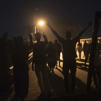 Silhouetted Sudanese protesters cross a bridge in Khartoum. They raise their hands in the air making peace signs.