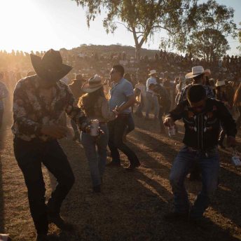 A crowd dances in a jaripeo arena at dusk