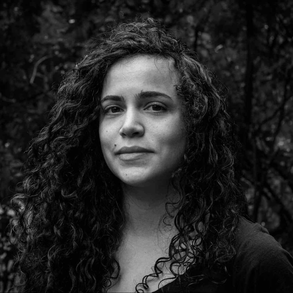 One of the producers for Matininó, a woman with curly long hair and a dark-colored shirt, poses for a black and white photo.