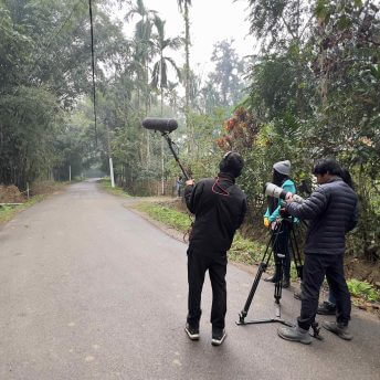 Film crew standing in the middle of the village road filming hoolock gibbons in the trees