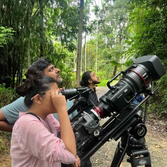 Film director Ragini looks through the camera viewfinder, while film crew members looks up at the Hoolock gibbon in the trees