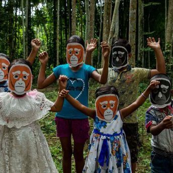 A group of children wearing Hoolock Gibbon face masks with hands in the air for celebration