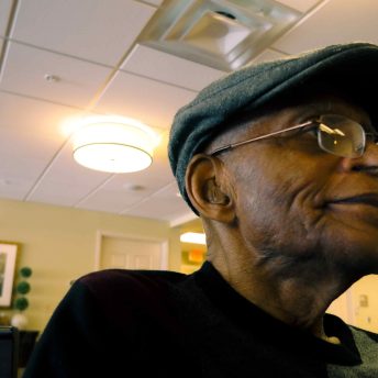 an older Black man with a gray hat and glasses looks off in the distance