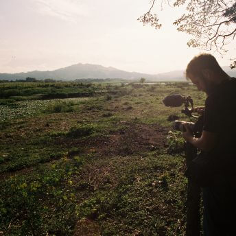 A man films a green, luscious landscape at dusk