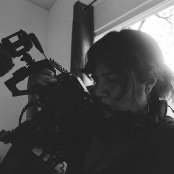 A woman holds a camera tightly and up close as she films