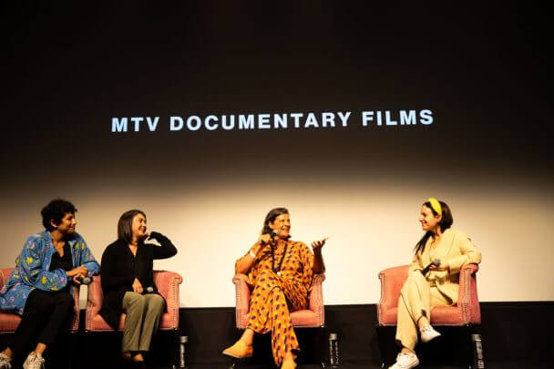 Q&A with filmmaker Maite Alberdi. From left to right: Translator, film participant Pauli, Moderator Kirsten Johnson, and filmmaker Maite Alberdi. They are all sitting in front of a screen.