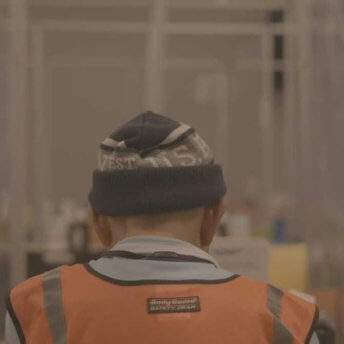 Still from Union. Back of the head of a man wearing a beanie and an orange vest.