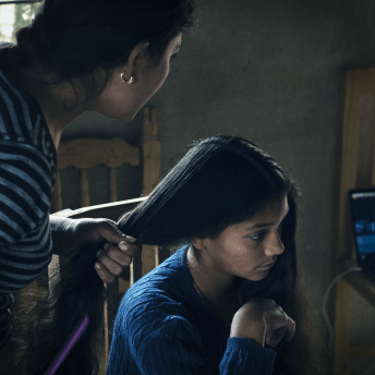 A little girl gets her hair done by an older woman.