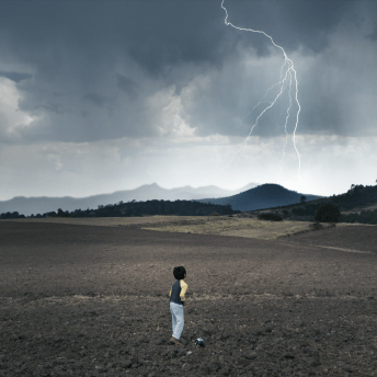 A boy looks off into the distance as lightning strikes a mountain nearby.