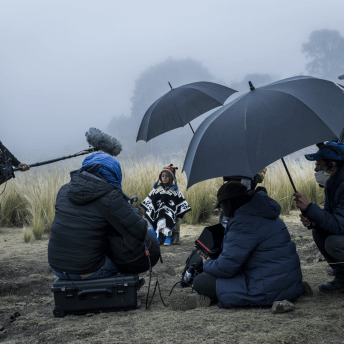 A camera crew films a child in the rain, holding umbrellas.
