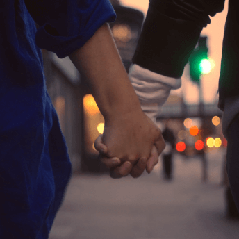 Two women hold hands, walking down the street at sunset.