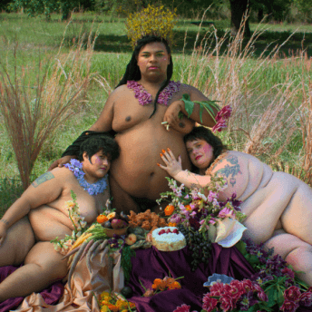 Three fat, gender non-conforming people of different races pose in the nude around a feast of cake and fried chicken. They are adorned with flowers.